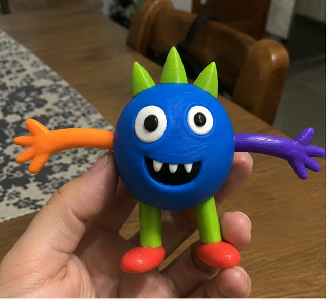 La figura del monstruo azul impresa en 3D, sostenida en una mano sobre una mesa